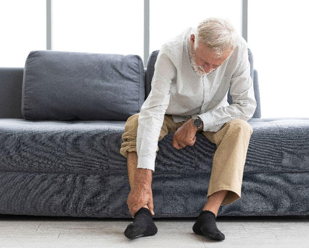 Elderly man sitting on sofa, grabbing ankle in pain